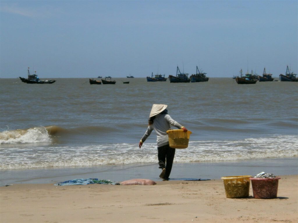 Vietnamese woman working on Mui Ne beach, with sea in the background.